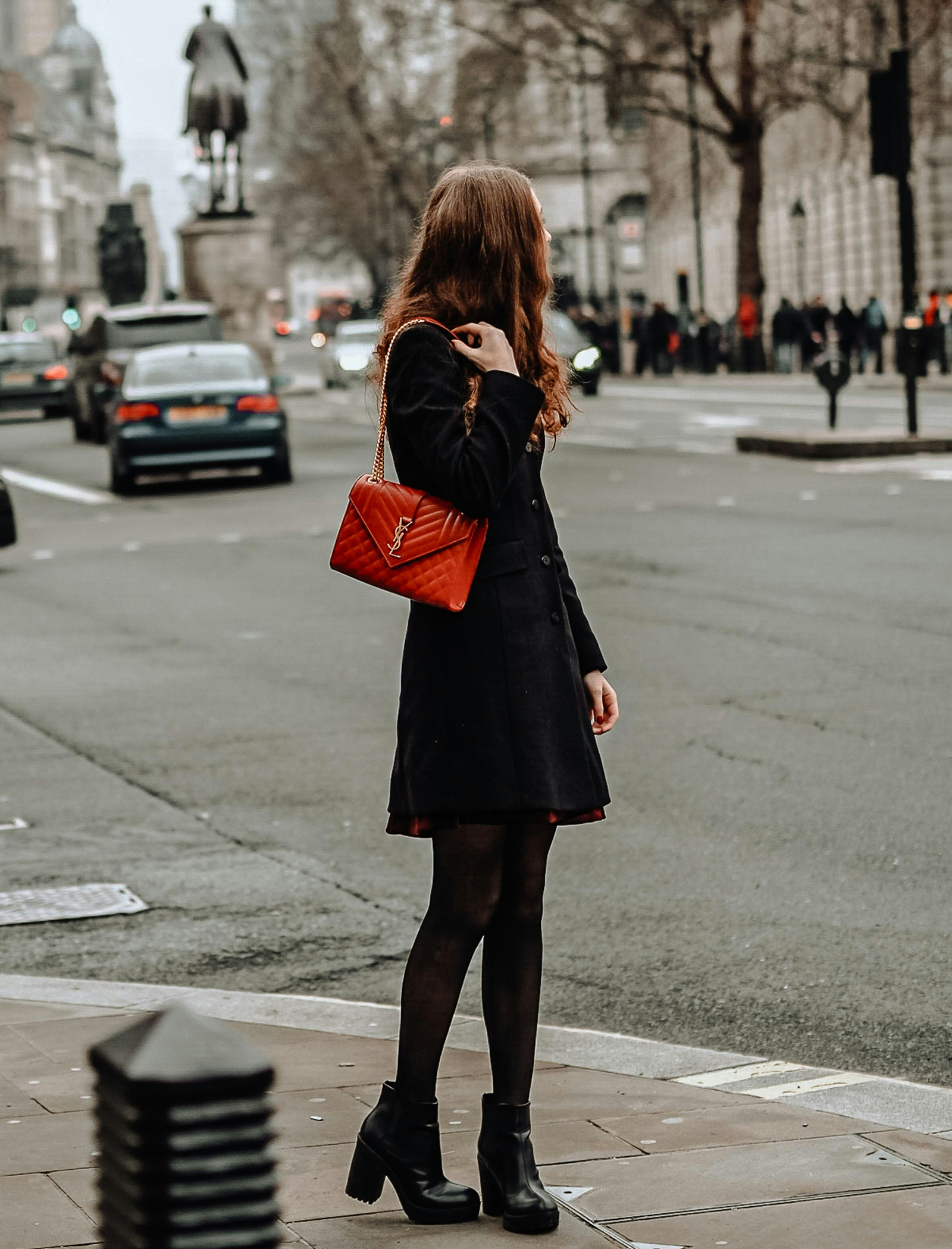 woman in black dress and red bag standing on the street corner